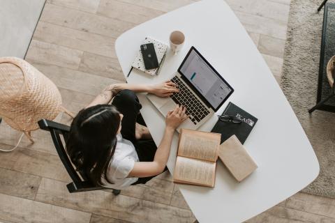 Mulher em uma mesa usando o notebook com caderno e celular. 